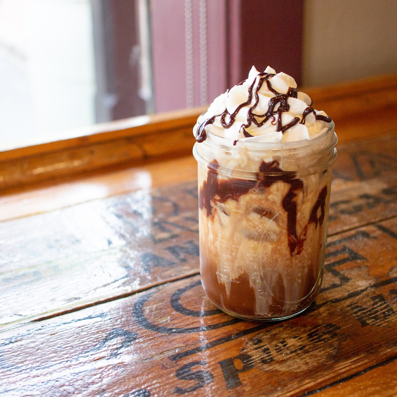Iced coffee with whipped cream and chocolate sauce on a wooden table.